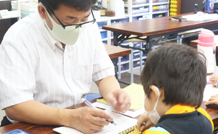 真剣な表情でそろばんに取り組むお子様の様子と、チラシに掲載された『3ヶ月で暗算がスッとできる』というキャッチコピーのイメージ画像