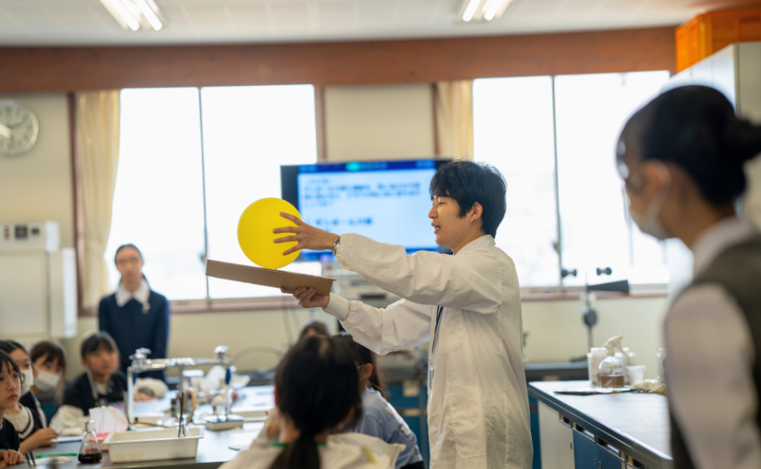 白衣を着た先生が黄色い風船を使って生き生きと理科の実験授業をしている様子