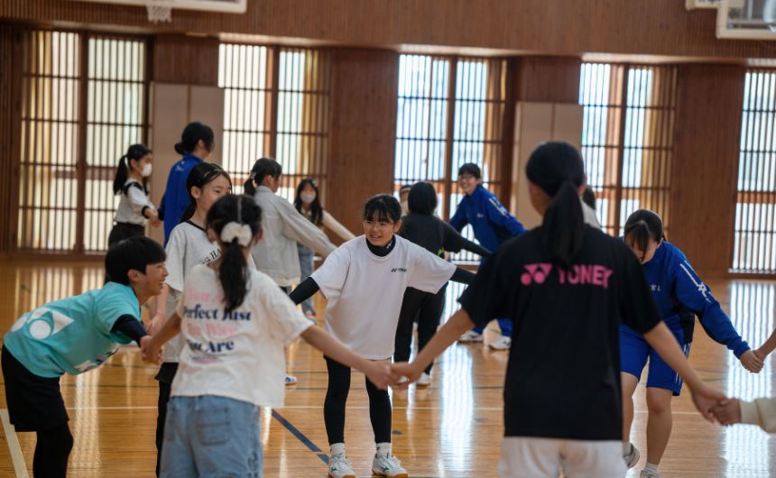 体育館で在校生と小学生が手をつないで体を動かしている楽しそうな様子
